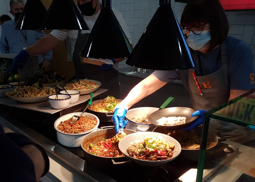 Cafeteria workers dish food onto plates.